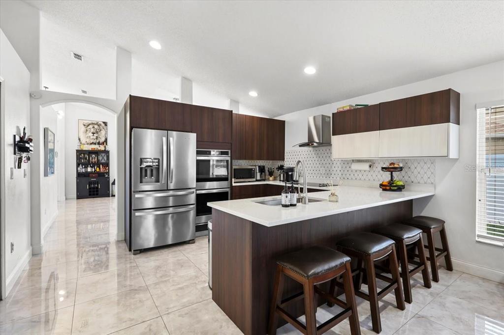 A modern kitchen features dark wood cabinetry, stainless steel appliances, and a white quartz island — 6847 BOUGANVILLEA CRESCENT DRIVE, ORLANDO, FL