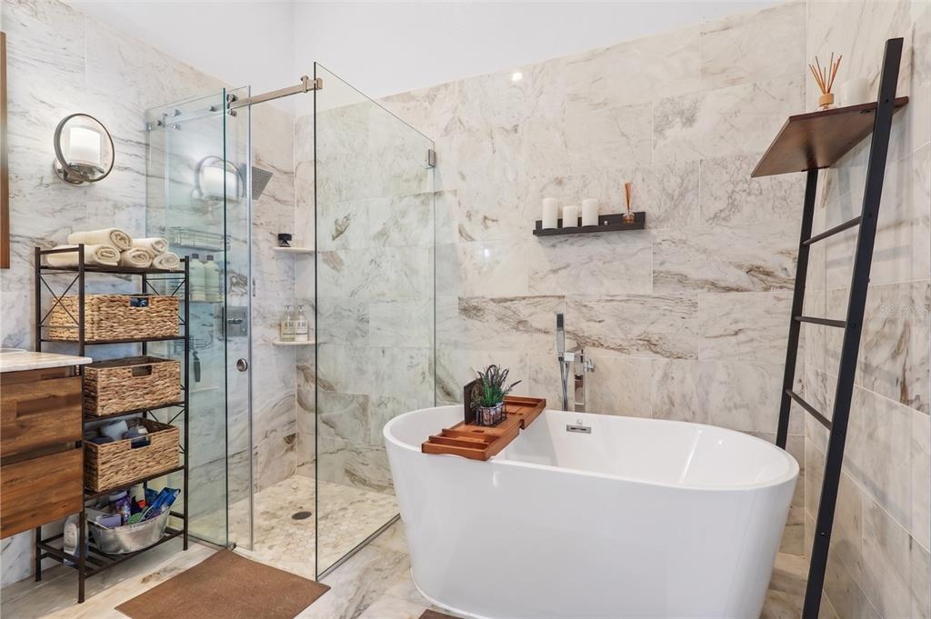 A bathroom features a glass-enclosed shower, a freestanding white tub, and marble-look wall tiles — 6847 BOUGANVILLEA CRESCENT DRIVE, ORLANDO, FL