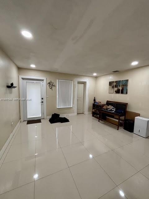 A bright, empty room features white tile flooring, recessed lighting, and a glass-paneled entry door — 7461 Douglas St, Hollywood FL 33024, HOLLYWOOD, FL