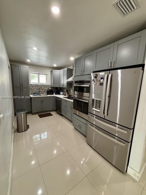 A modern kitchen features gray cabinetry, stainless steel appliances, and light-colored tile flooring — 7461 Douglas St, Hollywood FL 33024, HOLLYWOOD, FL