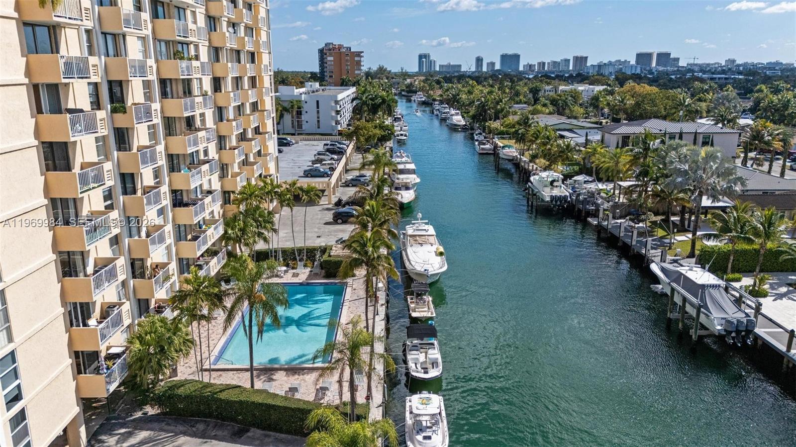 An aerial view shows a high-rise apartment building, a swimming pool, and boats docked canal-side — 2350 NE 135th St # 811, North Miami FL 33181, NORTH MIAMI, FL