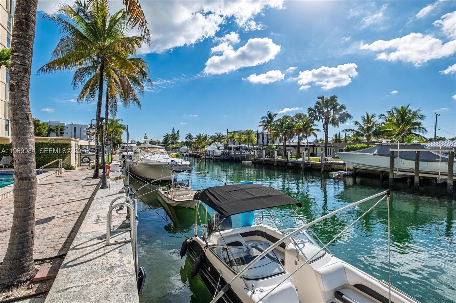 A canal view features several docked boats along a paved walkway lined with palm trees — 2350 NE 135th St # 811, North Miami FL 33181, NORTH MIAMI, FL