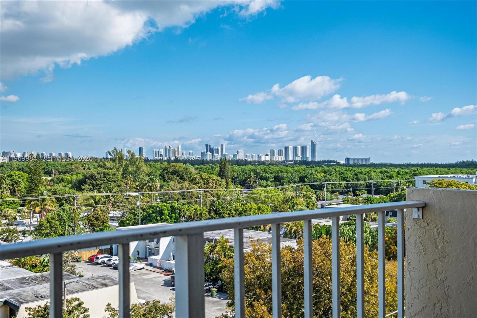 A balcony overlooks a lush green landscape with a distant city skyline under a blue sky — 2350 NE 135th St # 811, North Miami FL 33181, NORTH MIAMI, FL