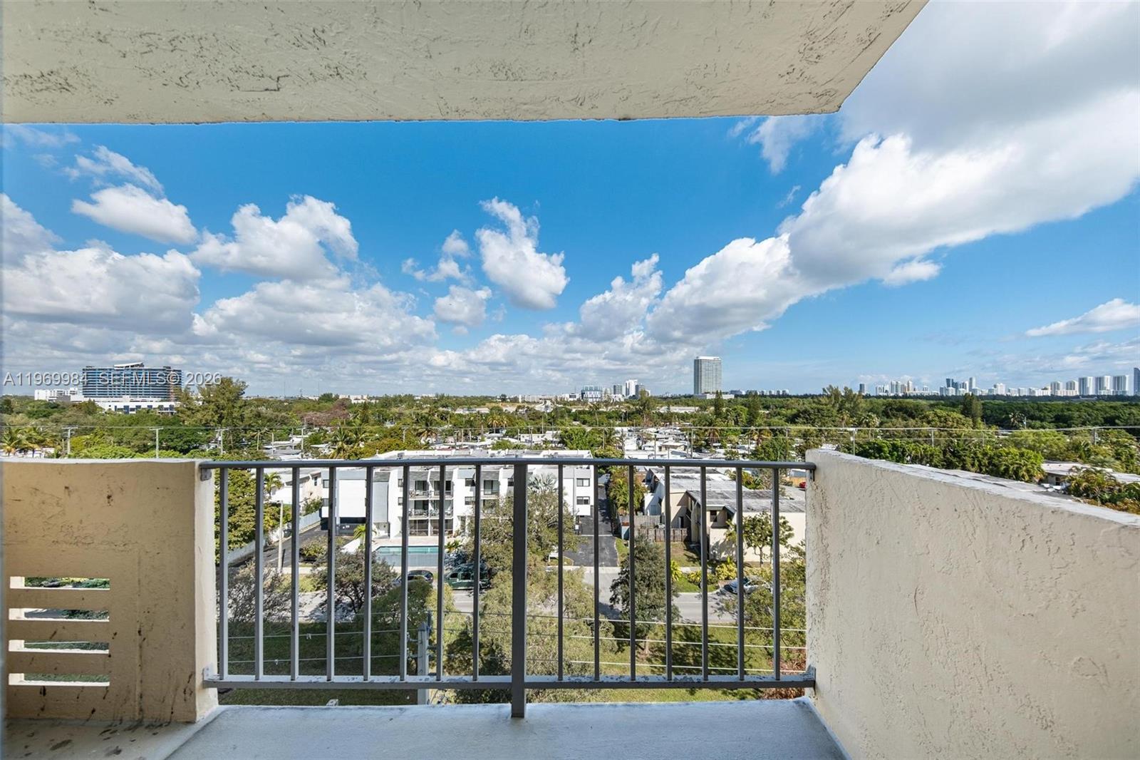 A balcony with a metal railing overlooks a suburban landscape under a cloudy blue sky — 2350 NE 135th St # 811, North Miami FL 33181, NORTH MIAMI, FL