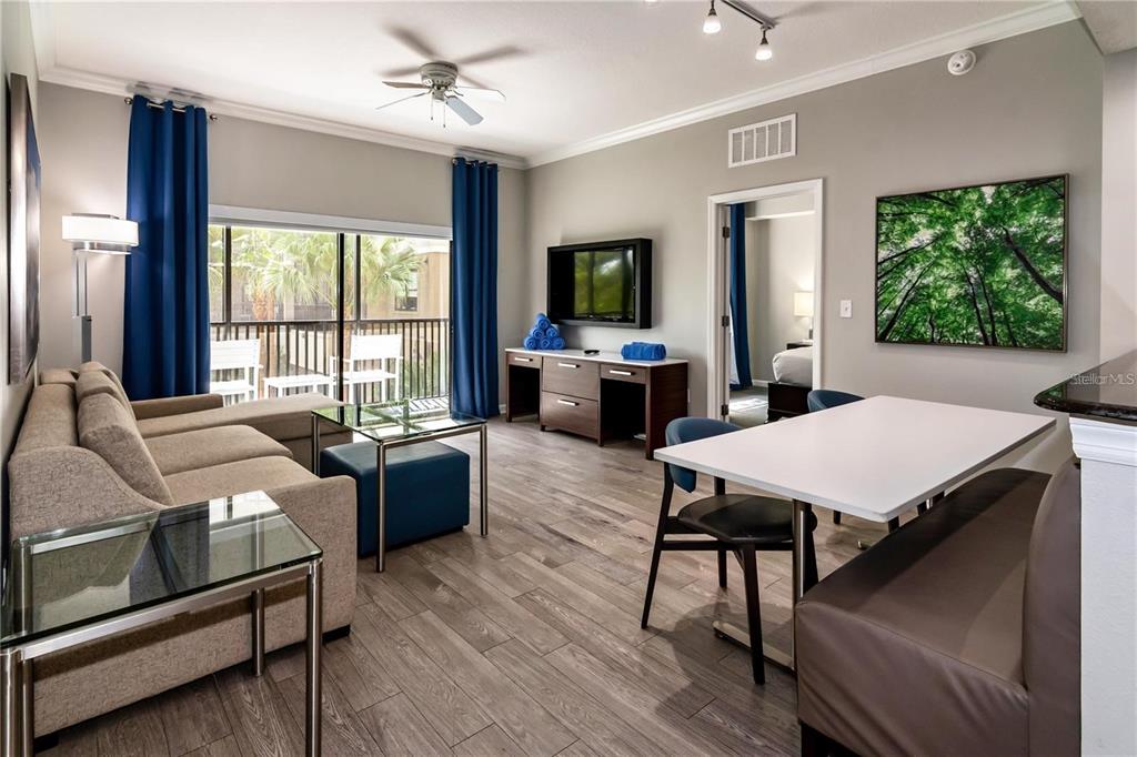 A living and dining area features wood-look flooring, a sofa, a television, and a balcony — 14501 GROVE RESORT AVENUE UNIT 1728, WINTER GARDEN, FL