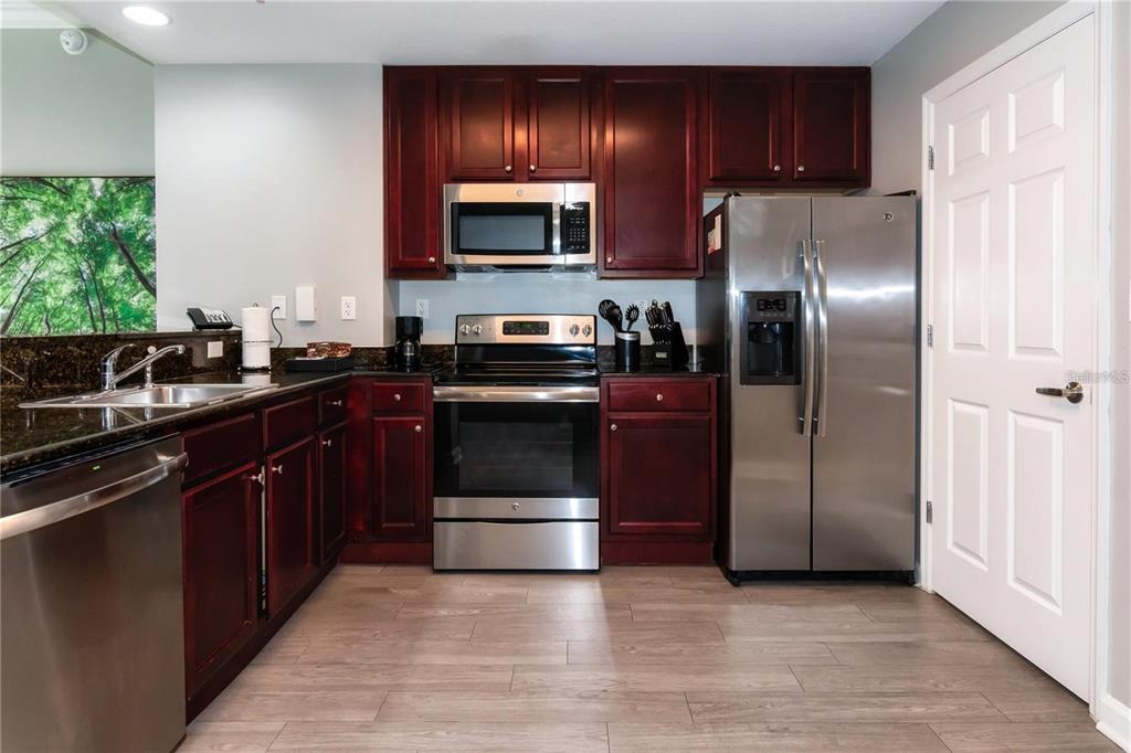 A kitchen features dark wood cabinets, stainless steel appliances, and dark countertops over wood-look flooring — 14501 GROVE RESORT AVENUE UNIT 1728, WINTER GARDEN, FL