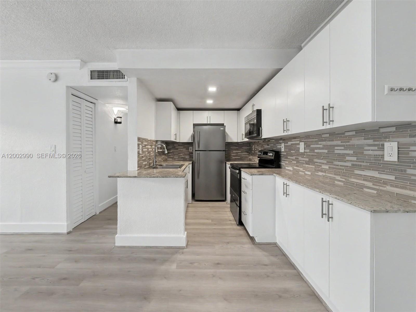 A kitchen features white cabinets, stainless steel appliances, granite countertops, and light wood-look flooring — 606 W 81st St # 120, Hialeah FL 33014, HIALEAH, FL