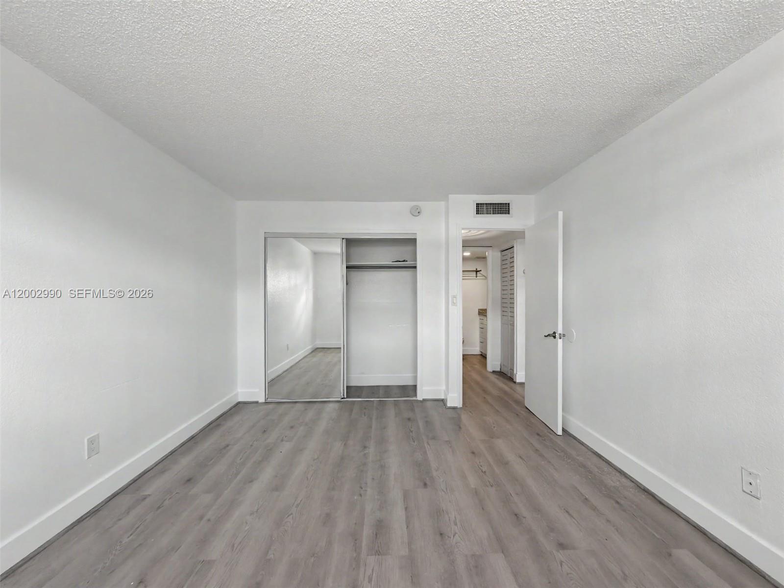 A bedroom with white walls, gray wood-look flooring, a mirrored closet, and an open doorway — 606 W 81st St # 120, Hialeah FL 33014, HIALEAH, FL