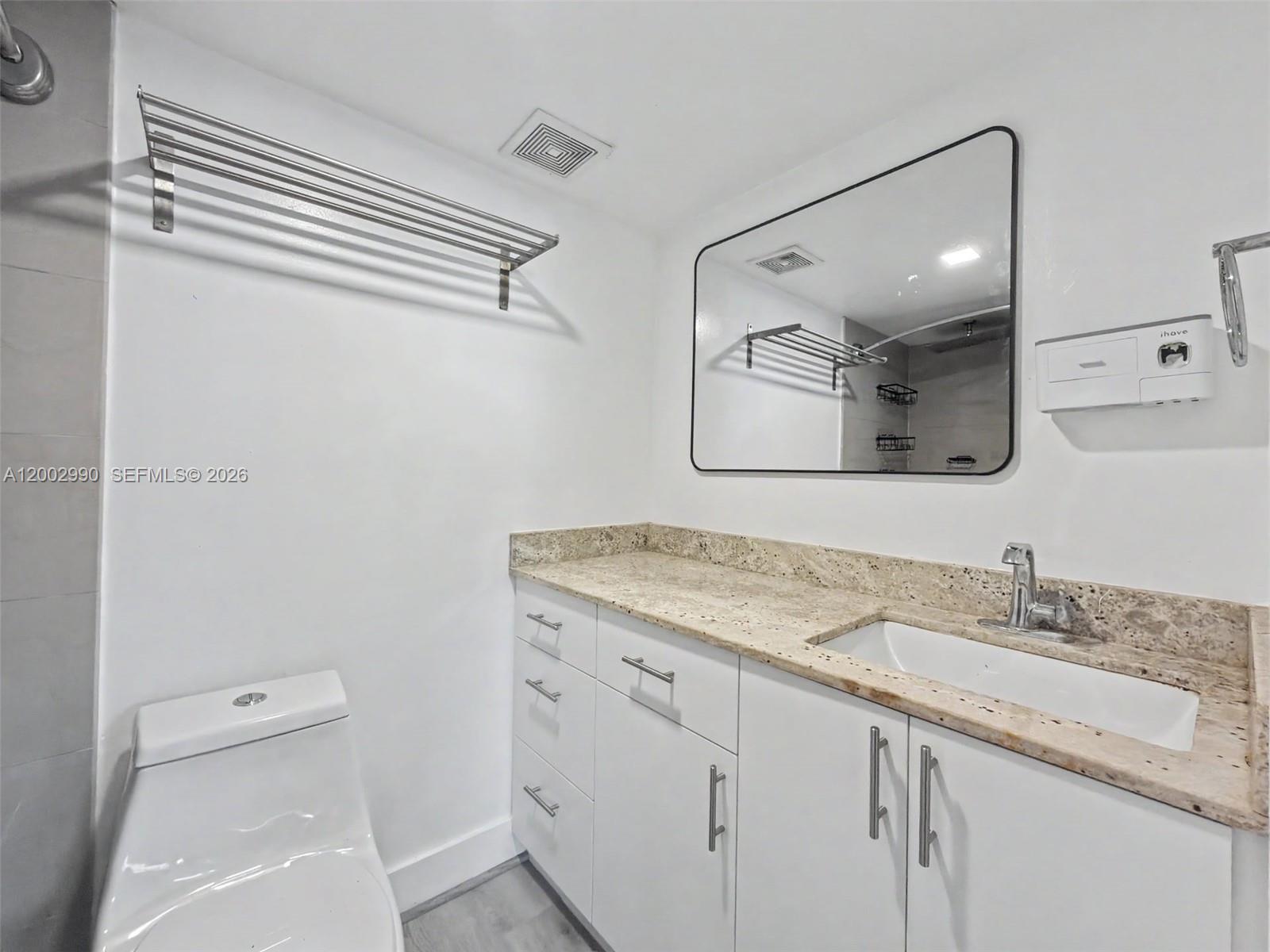 A bathroom features a white vanity with a granite countertop, a mirror, and a toilet — 606 W 81st St # 120, Hialeah FL 33014, HIALEAH, FL