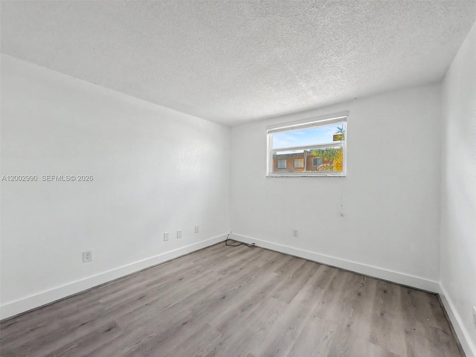 An empty bedroom features white walls, gray wood-look flooring, and a single window — 606 W 81st St # 120, Hialeah FL 33014, HIALEAH, FL