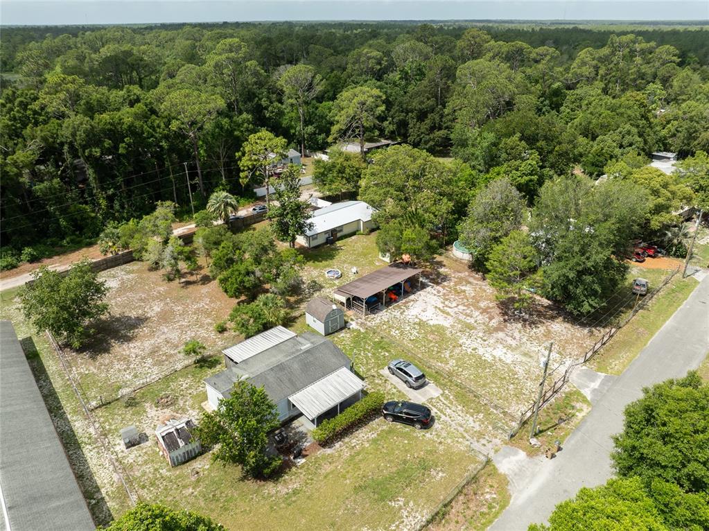 An aerial view shows a house with a carport, shed, and driveway on a wooded lot — 27751 LUELLA AVENUE, PAISLEY, FL