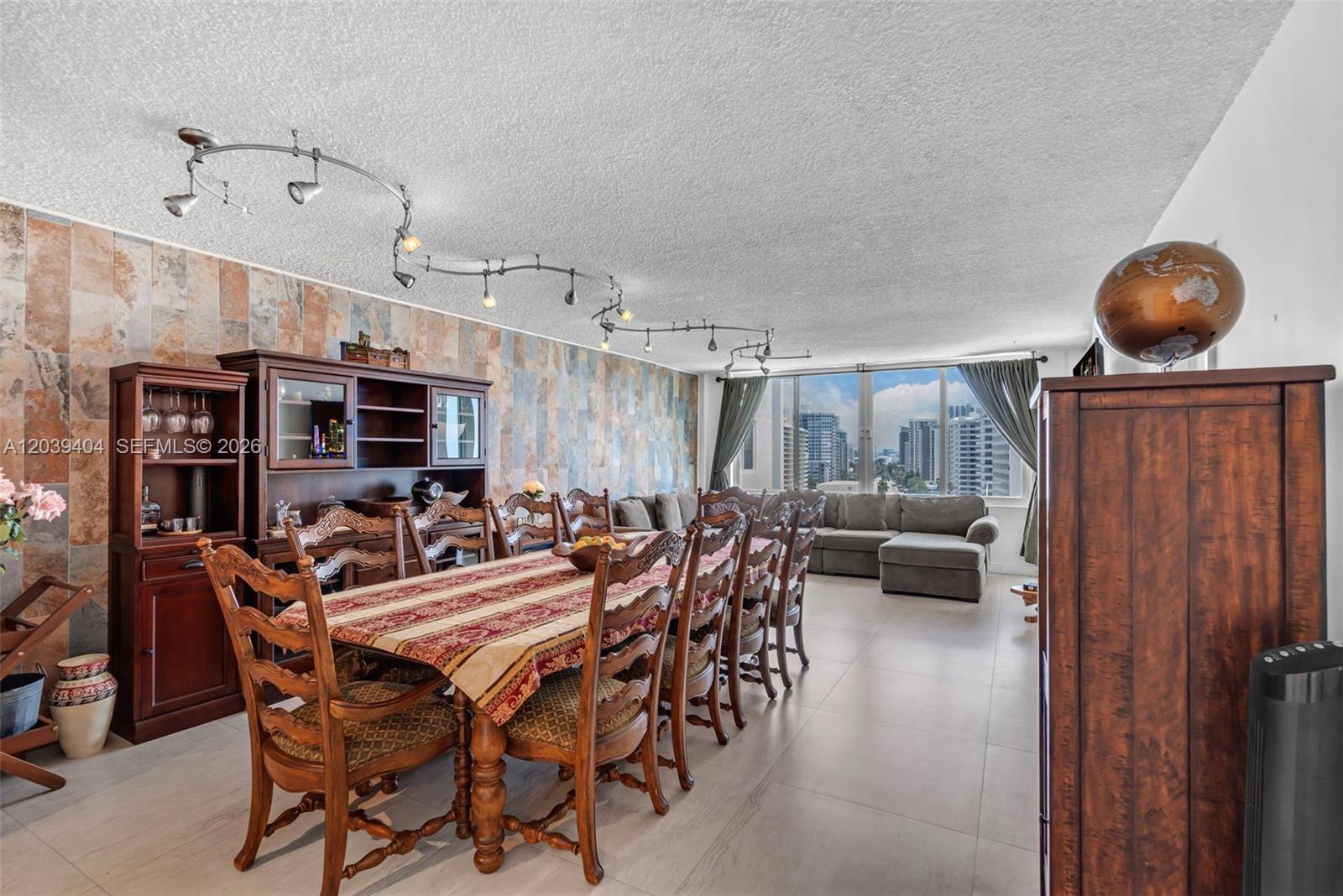 A dining room with a long wooden table, stone accent wall, and city view — 5401 Collins Ave # 813, Miami Beach FL 33140, MIAMI BEACH, FL