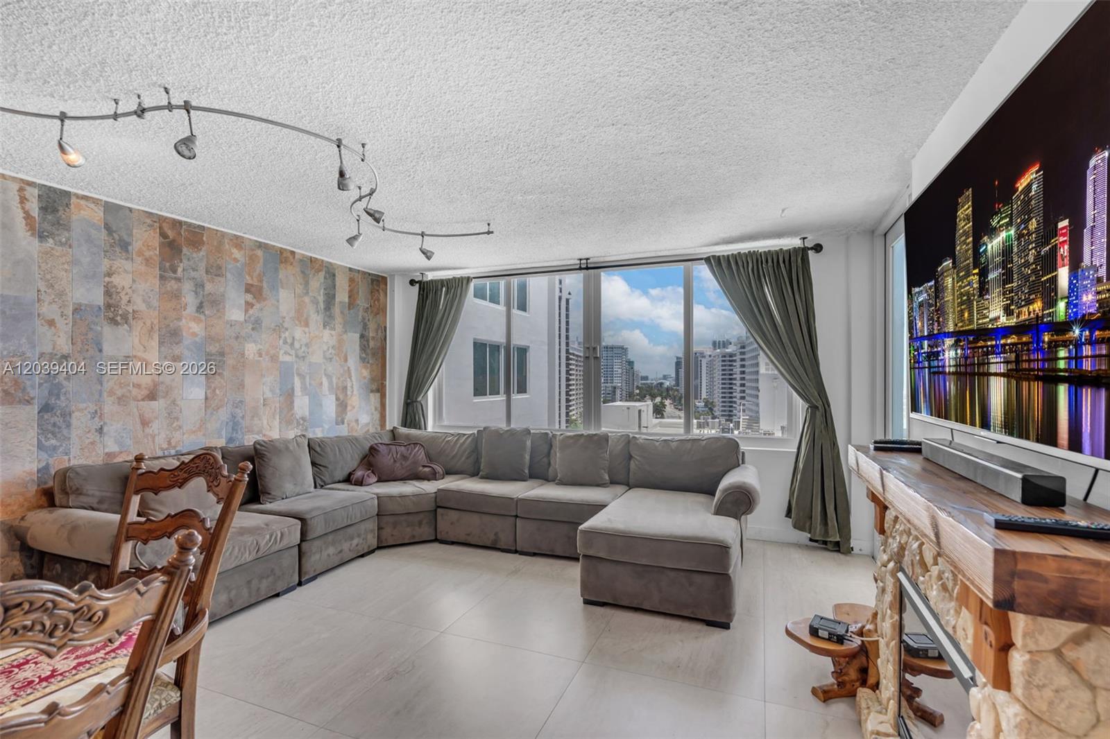 A living room features a large sectional sofa, stone-tiled accent wall, and a city view — 5401 Collins Ave # 813, Miami Beach FL 33140, MIAMI BEACH, FL