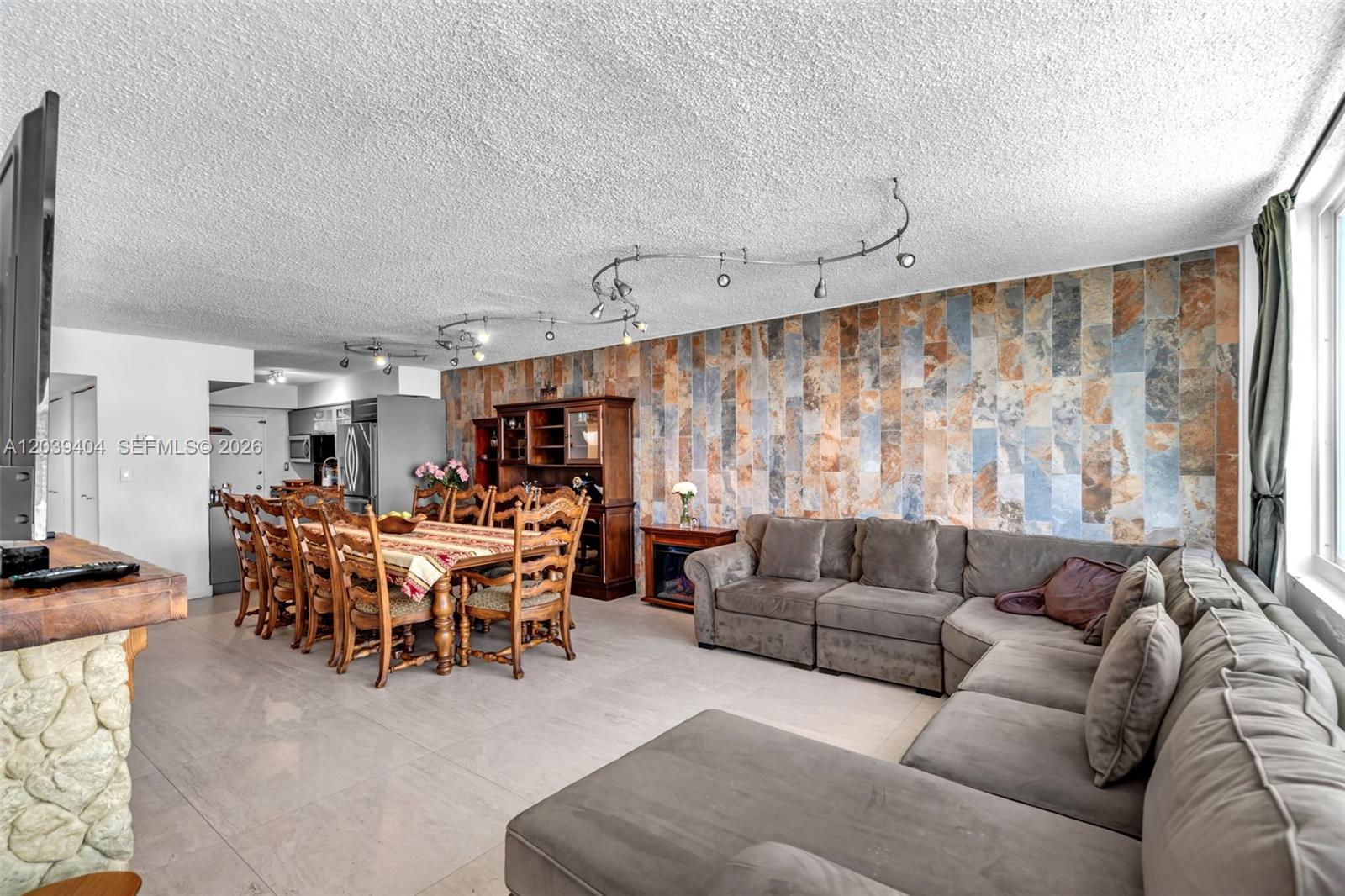 A living and dining room features a stone accent wall, track lighting, and tile flooring — 5401 Collins Ave # 813, Miami Beach FL 33140, MIAMI BEACH, FL