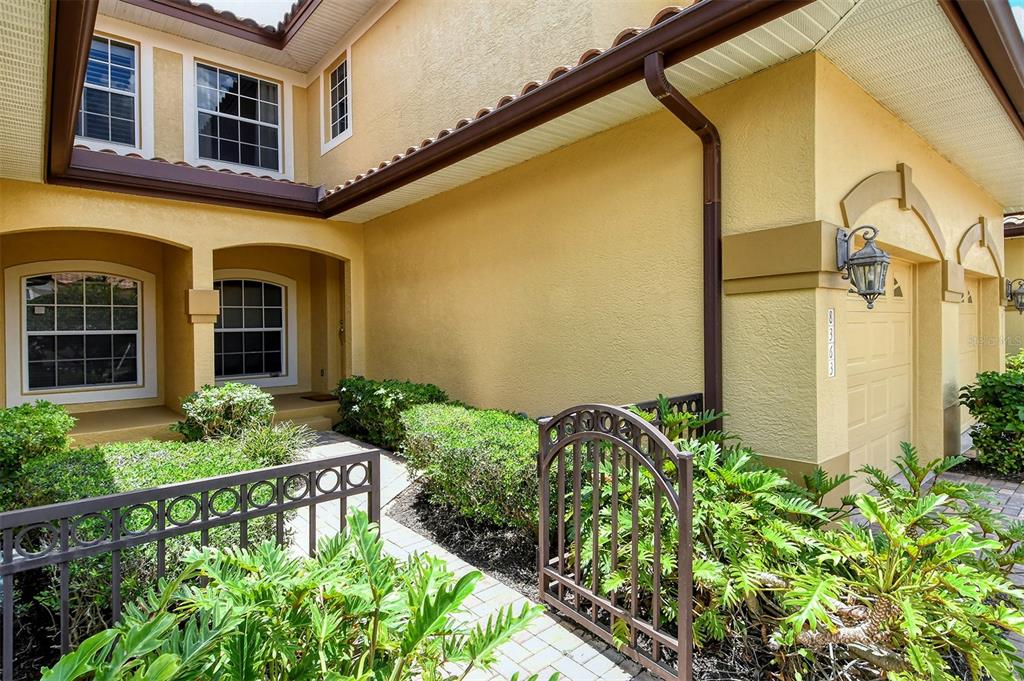 A yellow stucco house exterior features a gated walkway, arched windows, and a garage — 8363 MIRAMAR WAY UNIT 203, LAKEWOOD RANCH, FL