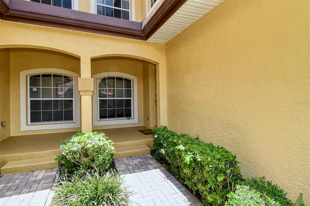 A paved walkway leads to the covered entryway of a yellow stucco house with arched windows — 8363 MIRAMAR WAY UNIT 203, LAKEWOOD RANCH, FL