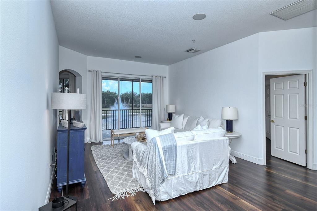A living room features dark wood floors, white furniture, and a sliding door to a balcony — 8363 MIRAMAR WAY UNIT 203, LAKEWOOD RANCH, FL