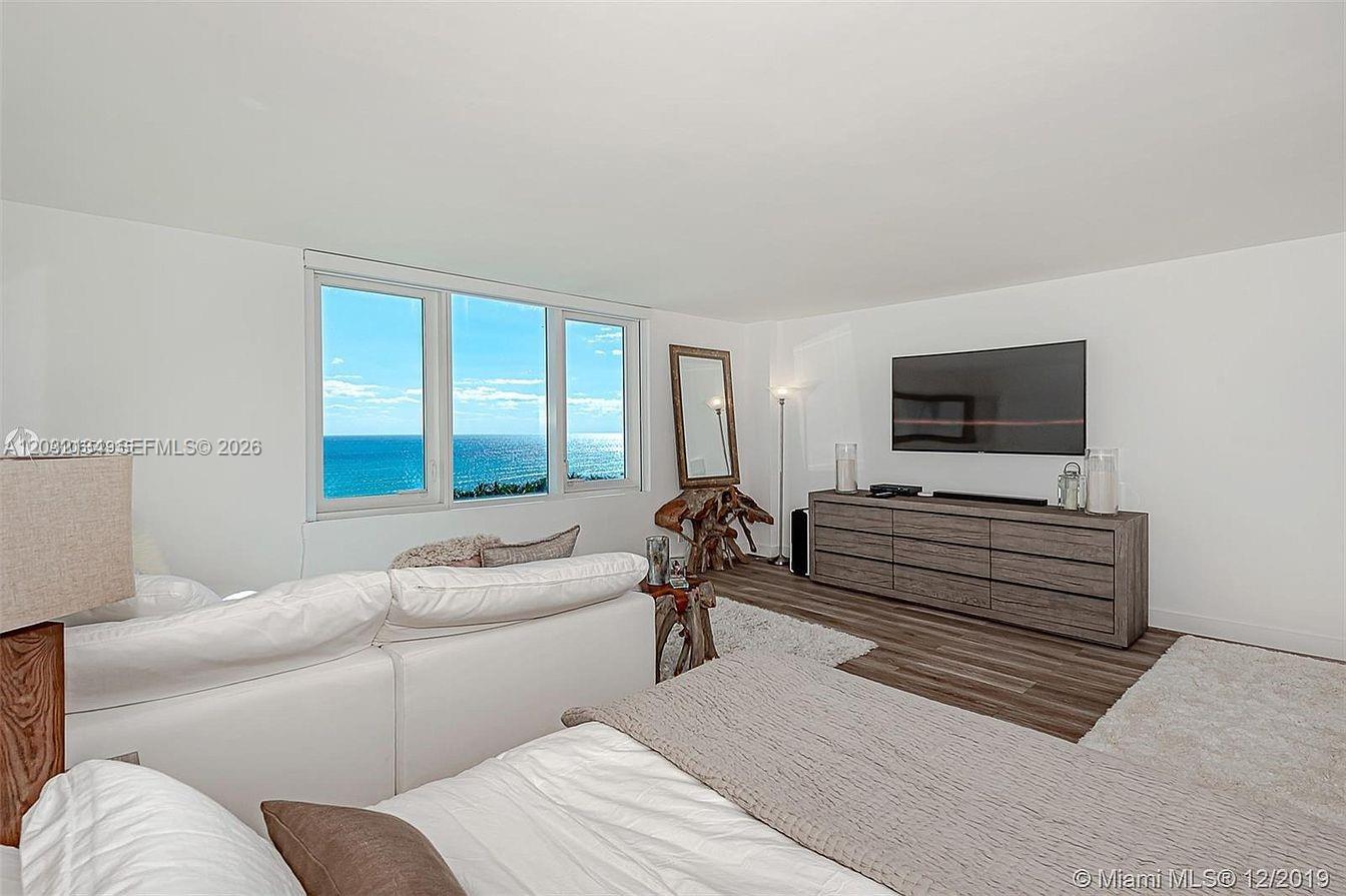 A bedroom features a white bed, a wooden dresser with a television, and ocean views — 2301 Collins Ave # 843, Miami Beach FL 33139, MIAMI BEACH, FL