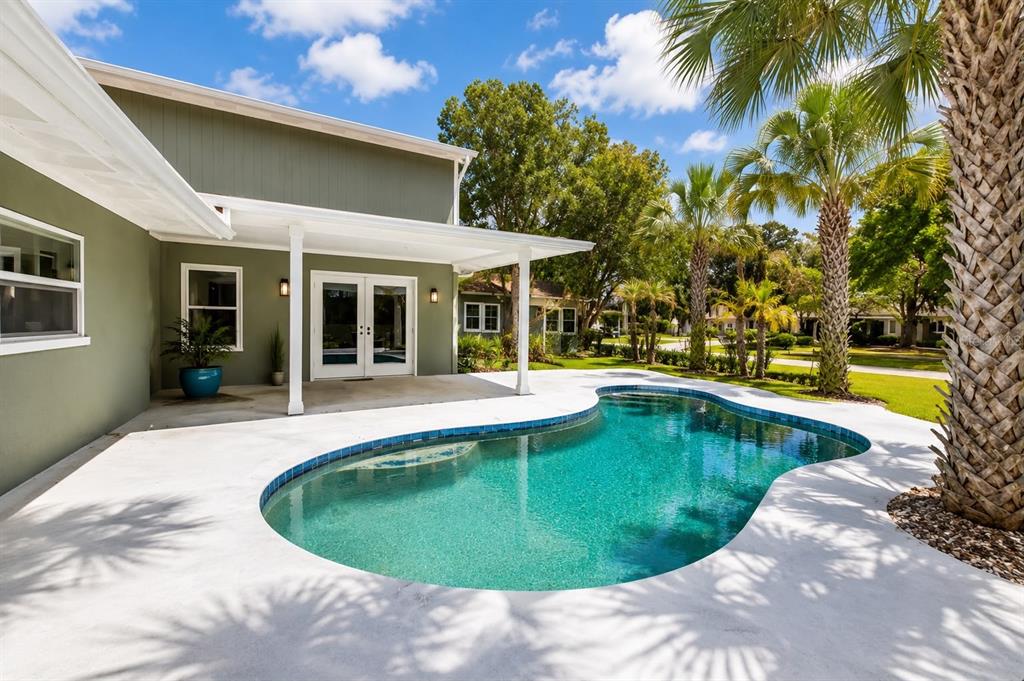 A green house with a covered patio and a kidney-shaped swimming pool in the backyard — 26 BACKSPIN LANE, ORLANDO, FL