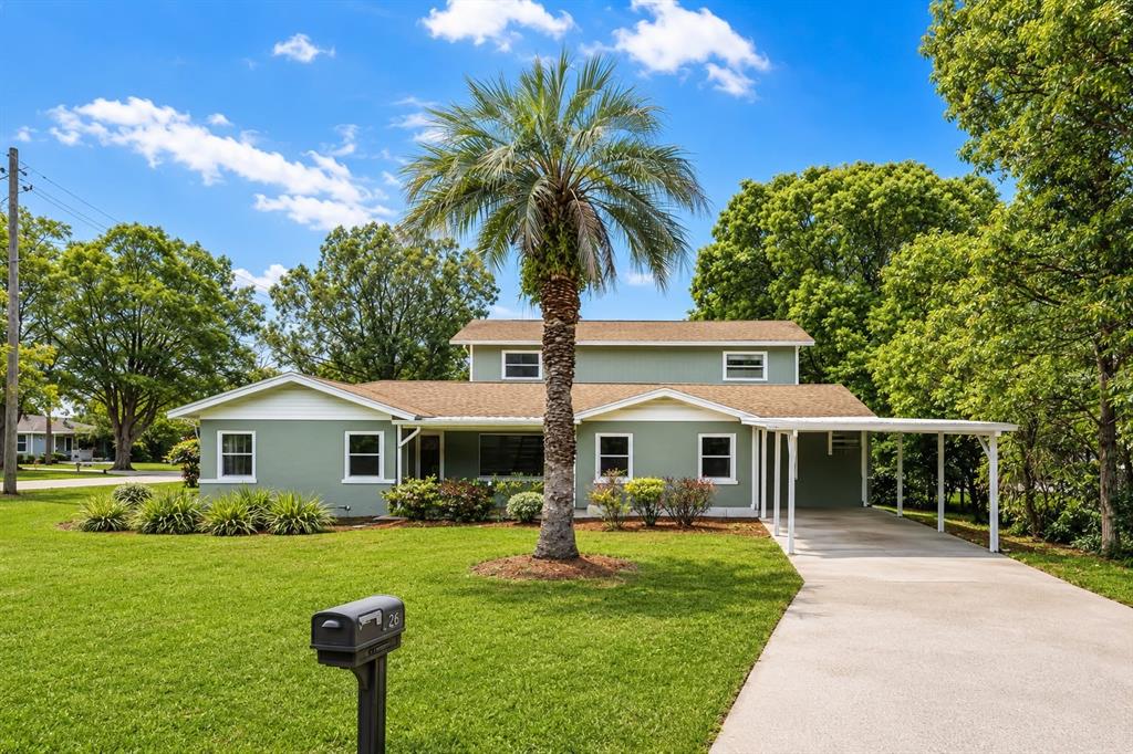 A green, two-story house with a palm tree in the front yard and a carport — 26 BACKSPIN LANE, ORLANDO, FL