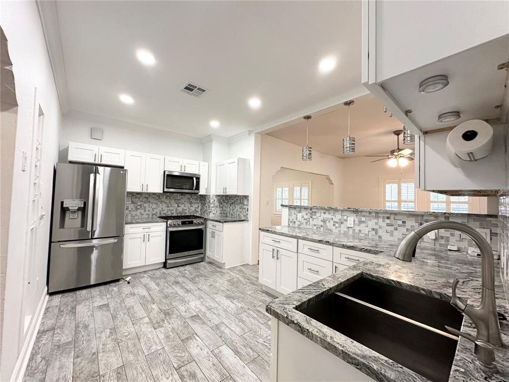 A modern kitchen features white cabinets, granite countertops, stainless steel appliances, and gray wood-look flooring — 3025 W NORTH A STREET, TAMPA, FL