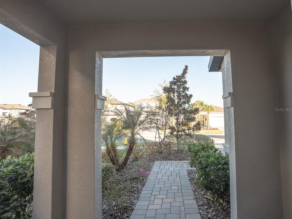 A view from a covered porch looking out toward a paved walkway and suburban landscaping — 5836 TIMBERDALE AVENUE, WESLEY CHAPEL, FL