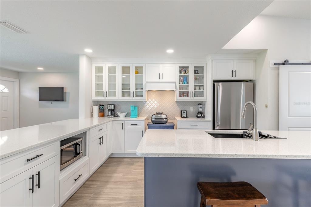 A modern kitchen features white cabinetry, a blue island with a sink, and quartz countertops — 8 ROBBEN TERRACE, DAYTONA BEACH, FL
