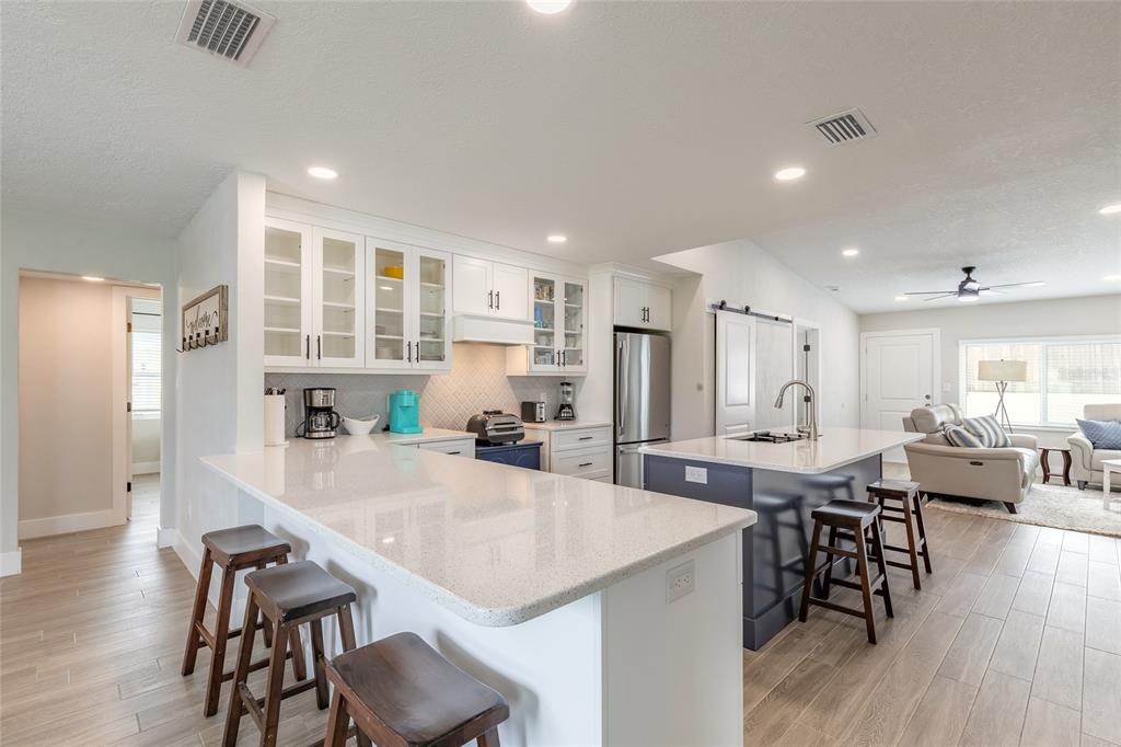 A kitchen features white cabinetry, a quartz-topped peninsula, a dark blue island, and wood-look flooring — 8 ROBBEN TERRACE, DAYTONA BEACH, FL