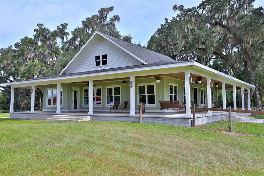 A light green house with a wrap-around porch and a metal roof under oak trees — 8410 NE 155TH AVENUE, WILLISTON, FL