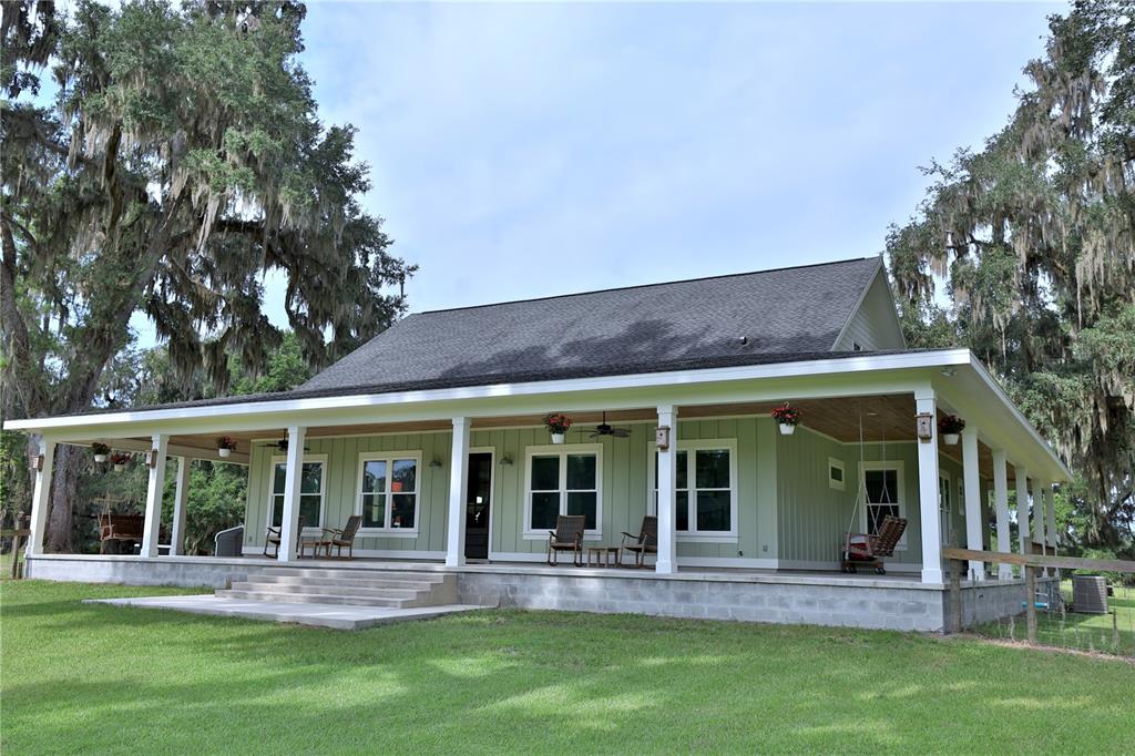 A light green house with a large wrap-around porch and a dark shingled roof — 8410 NE 155TH AVENUE, WILLISTON, FL