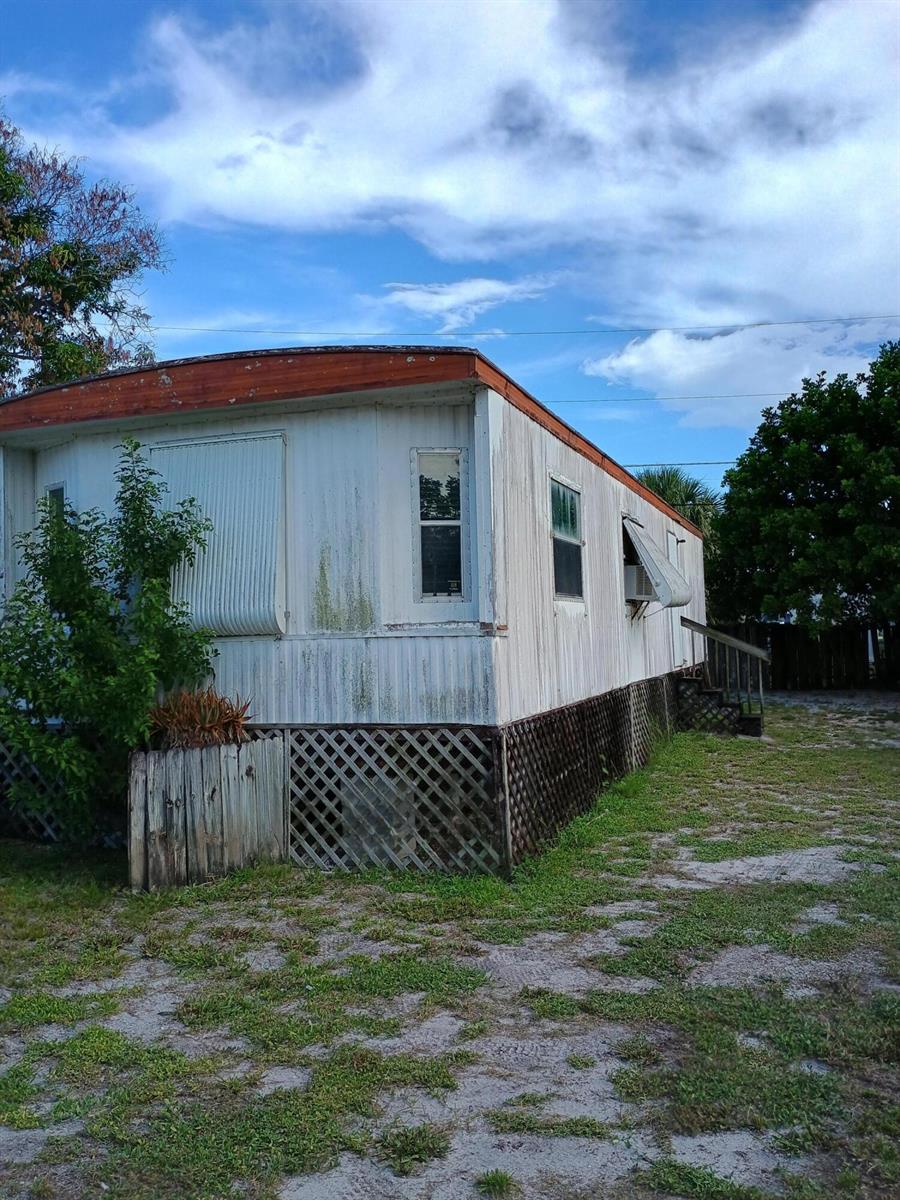 An exterior view of a weathered mobile home with lattice skirting and a small staircase — 7930 SE Cactus Trail, Hobe Sound FL 33455, HOBE SOUND, FL