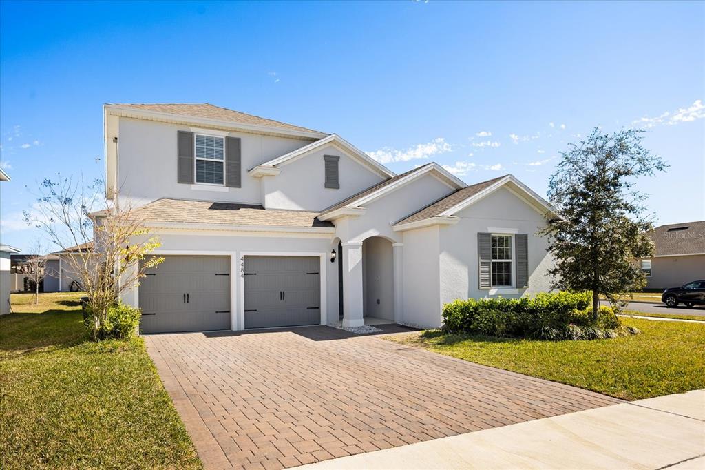 A two-story house with a light-colored stucco exterior, gray garage doors, and a paved driveway — 4484 LIONS GATE AVENUE, CLERMONT, FL