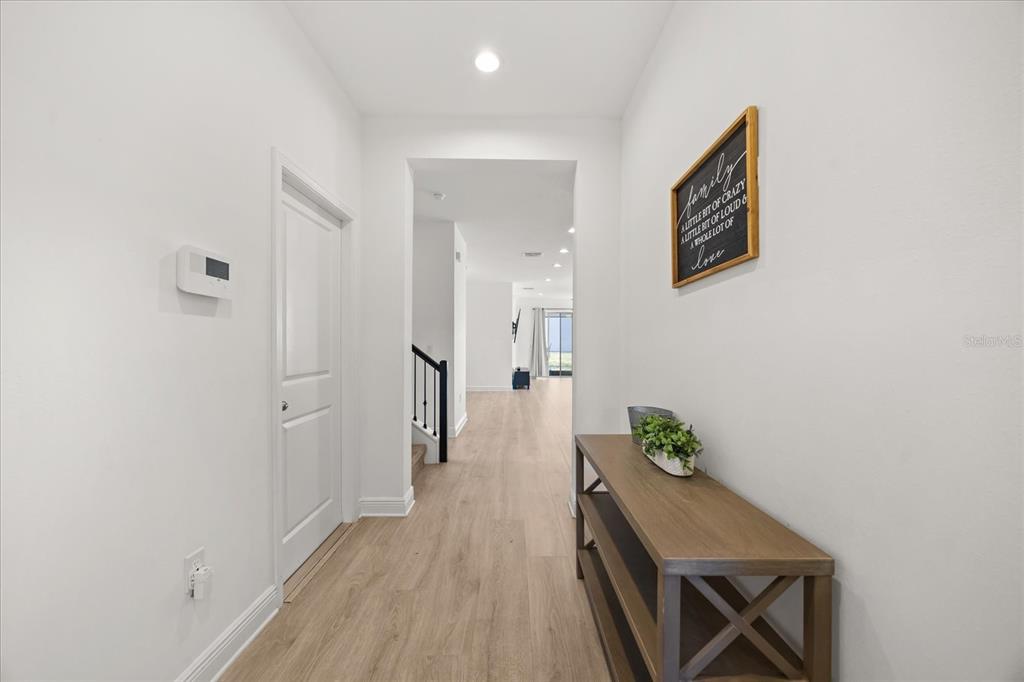 A bright hallway features light wood-look flooring, a console table, and a wall-mounted sign — 4484 LIONS GATE AVENUE, CLERMONT, FL