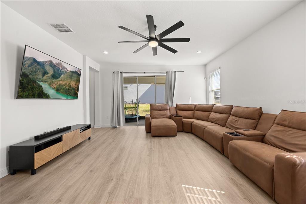 A living room features light wood-look flooring, a brown sectional sofa, and a wall-mounted television — 4484 LIONS GATE AVENUE, CLERMONT, FL