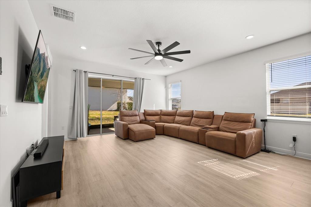 A living room features light wood flooring, a large brown sectional sofa, and a ceiling fan — 4484 LIONS GATE AVENUE, CLERMONT, FL