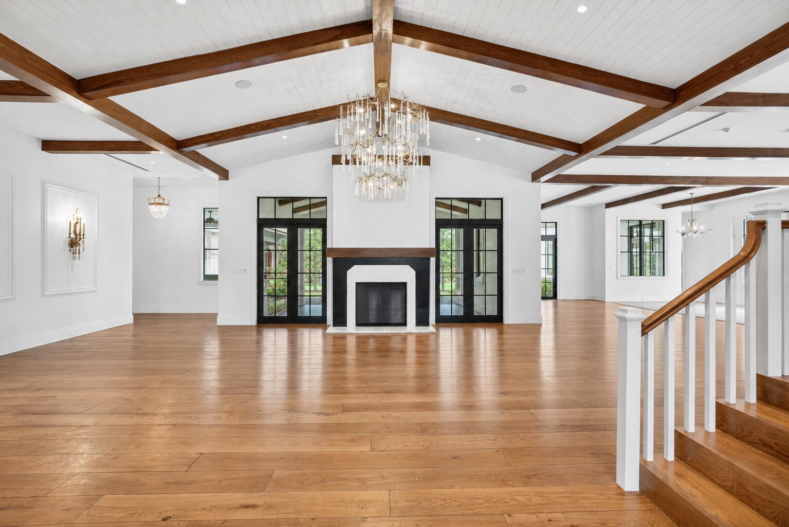 A spacious living room features a vaulted ceiling with wood beams and a central fireplace — 10250 El Paraiso Place, Delray Beach FL 33446, DELRAY BEACH, FL