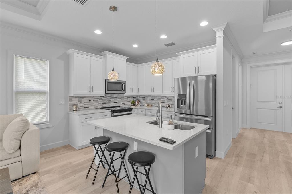 A modern kitchen features white cabinetry, a gray island with bar stools, and stainless steel appliances — 1497 NORDENDALE BOULEVARD, NORTH PORT, FL