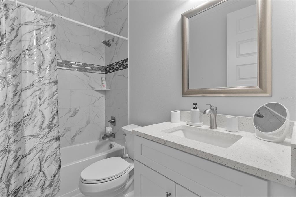 A bathroom features a white vanity, a marble-tiled shower-tub combination, and a framed wall mirror — 1497 NORDENDALE BOULEVARD, NORTH PORT, FL