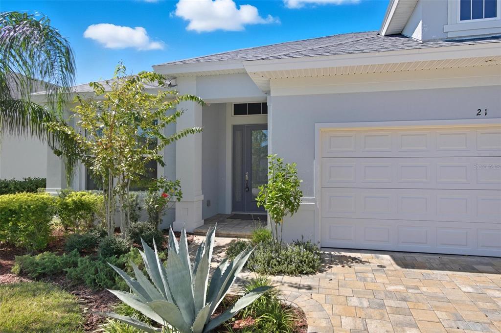 A single-story house exterior with a gray front door, white garage, and landscaped front yard — 21 SPRING STREET, PALM COAST, FL