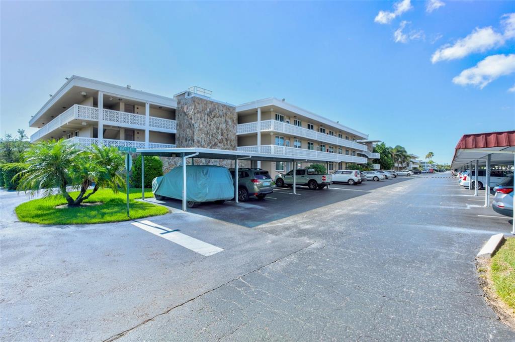A multi-story apartment building features covered parking spaces and a stone-accented exterior wall — 5095 BAY STREET NE UNIT 310, ST PETERSBURG, FL