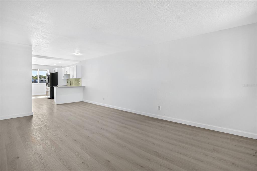 A bright, open-concept living area features light wood-look flooring and a view into the kitchen — 5095 BAY STREET NE UNIT 310, ST PETERSBURG, FL