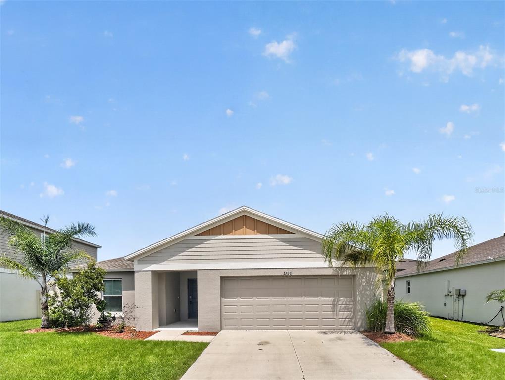 A single-story house with a two-car garage, light siding, and palm trees in the yard — 5936 SLATE ROCK DRIVE, LAKELAND, FL
