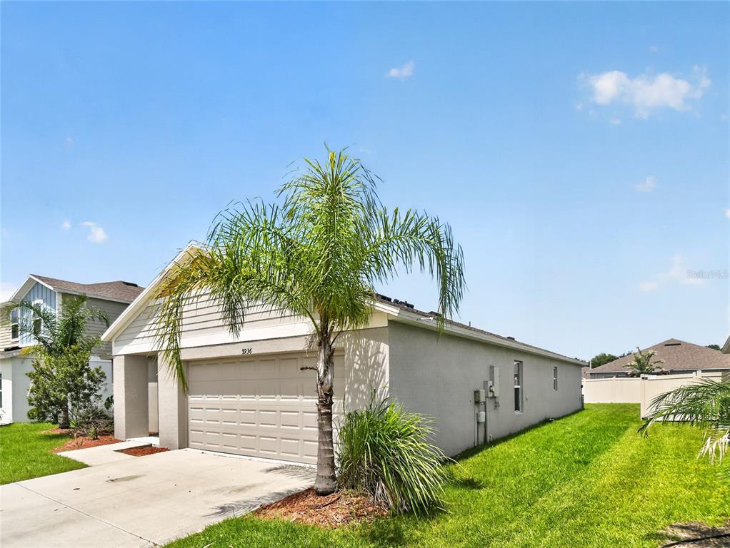 A single-story house with a beige stucco exterior, a two-car garage, and a palm tree — 5936 SLATE ROCK DRIVE, LAKELAND, FL