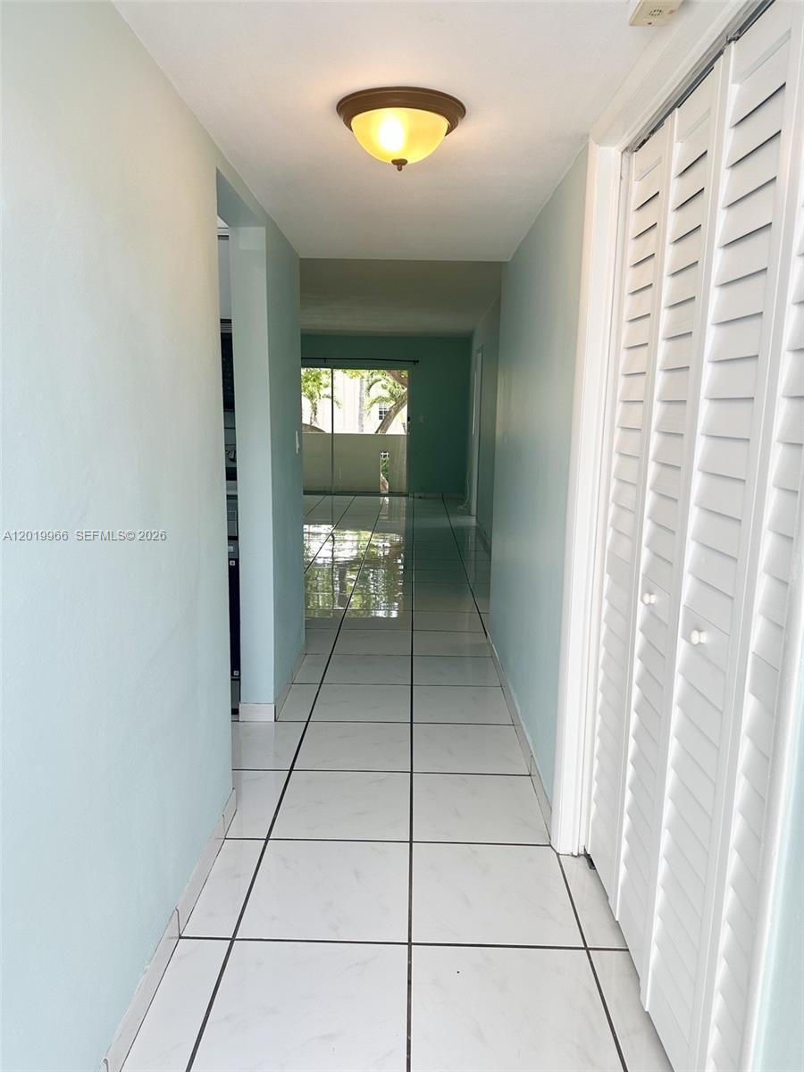 A hallway with white tiled flooring leads toward a room with a sliding glass door — 300 Galen Dr # 206, Key Biscayne FL 33149, KEY BISCAYNE, FL