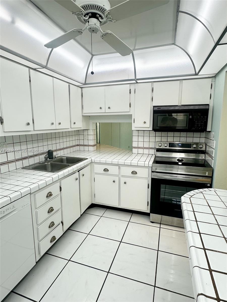 A kitchen features white cabinets, tiled countertops, a stainless steel stove, and a ceiling fan — 300 Galen Dr # 206, Key Biscayne FL 33149, KEY BISCAYNE, FL