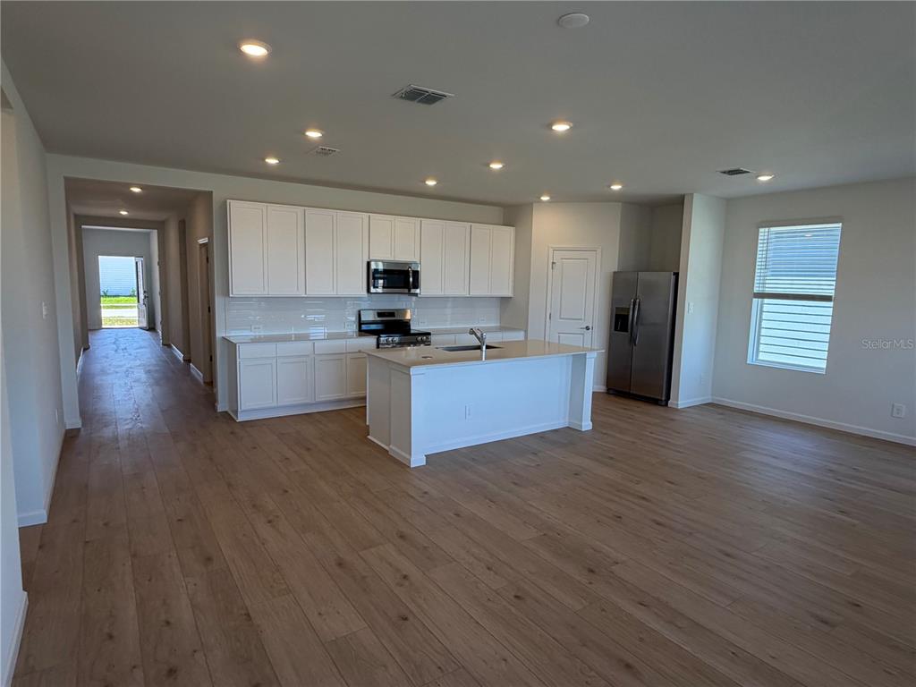 A modern kitchen features white cabinets, stainless steel appliances, and an island with wood flooring — 4377 VIBERNUM AVENUE UNIT A, ST CLOUD, FL
