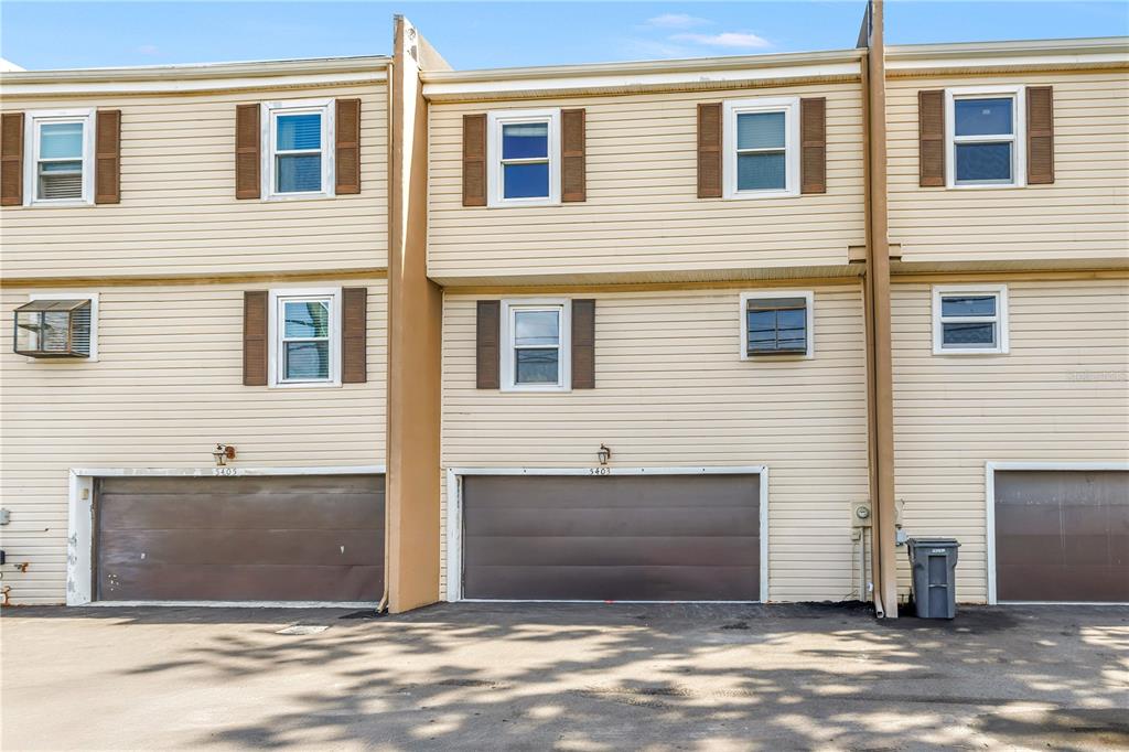 A row of three-story townhouses with beige siding, brown garage doors, and brown shutters — 5403 SWEETWATER TERRACE CIRCLE UNIT 5403, TAMPA, FL