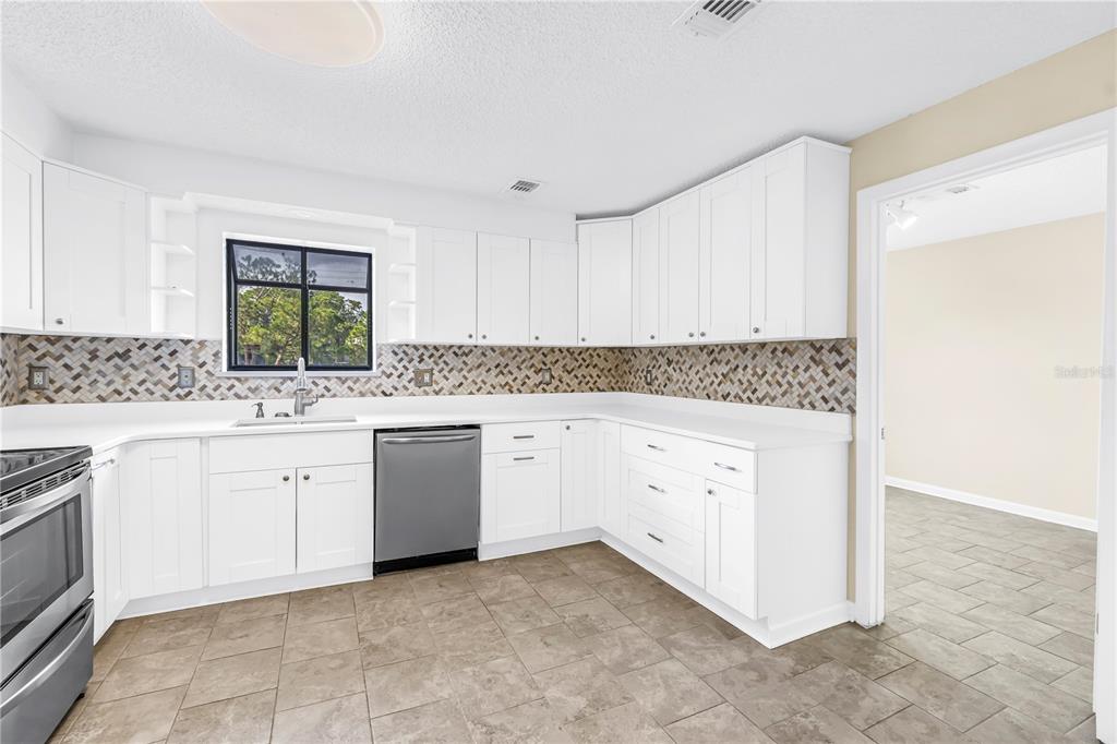 A kitchen features white cabinets, a mosaic tile backsplash, stainless steel appliances, and tiled flooring — 5403 SWEETWATER TERRACE CIRCLE UNIT 5403, TAMPA, FL