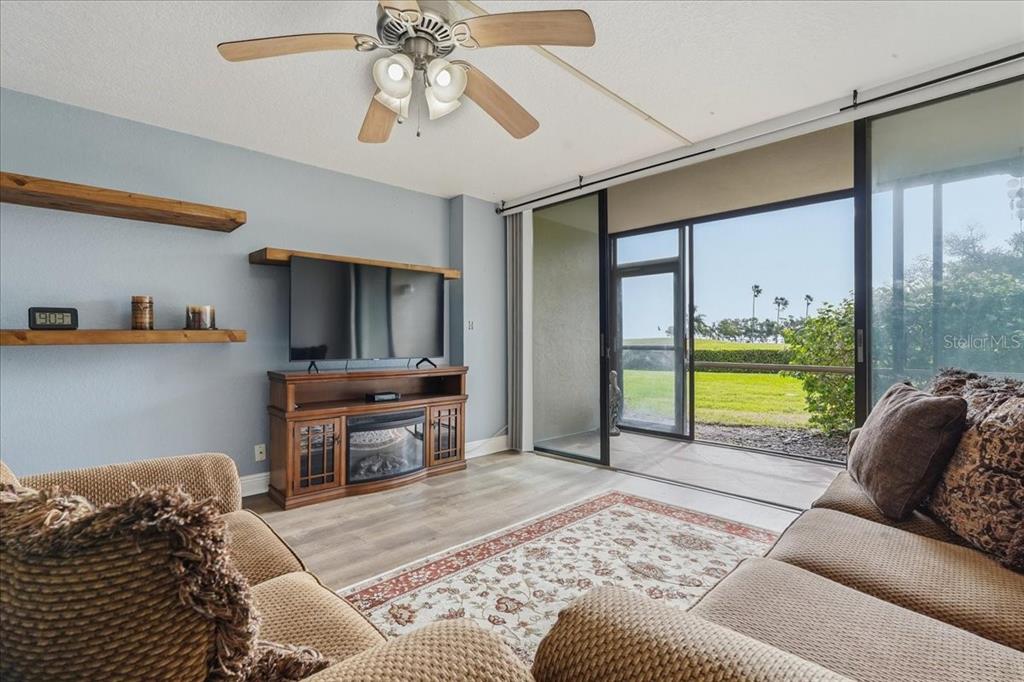 A living room features a ceiling fan, wood-look flooring, a television console, and sliding glass doors — 2616 COVE CAY DRIVE UNIT 105, CLEARWATER, FL