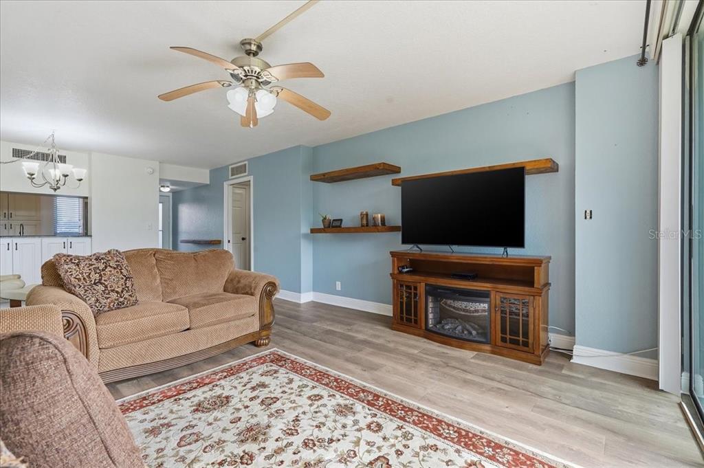 A living room features light blue walls, wood-look flooring, a ceiling fan, and a television console — 2616 COVE CAY DRIVE UNIT 105, CLEARWATER, FL